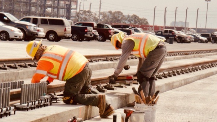 Two workers in high-visibility gear laying rail track at a port terminal